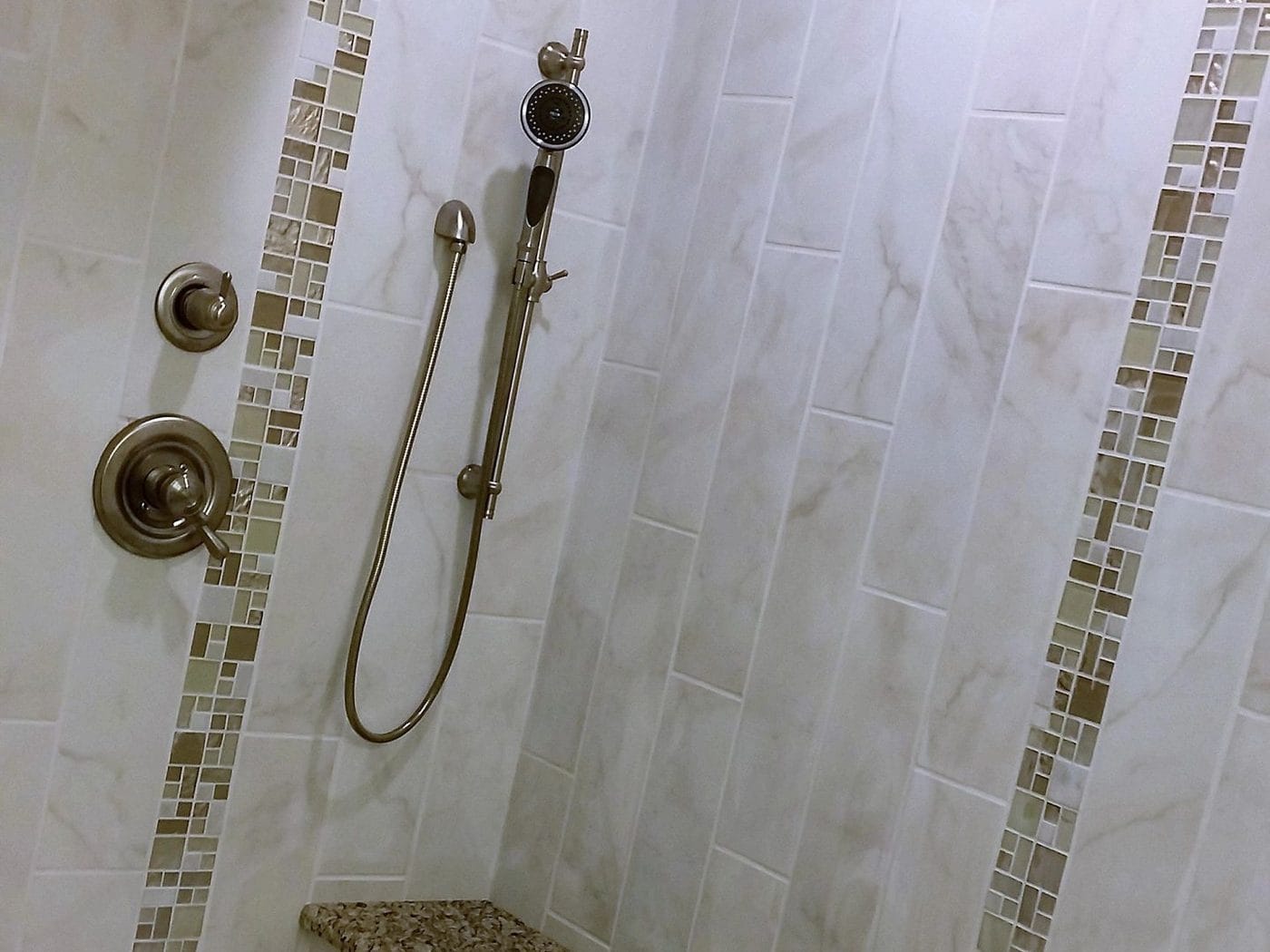 A shower with a mosaic tile strip and a stone bench