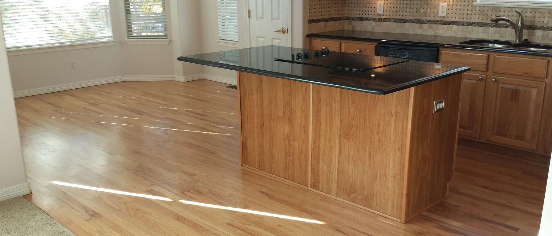 A wide view of a finished kitchen and living space with an island and hardwood flooring
