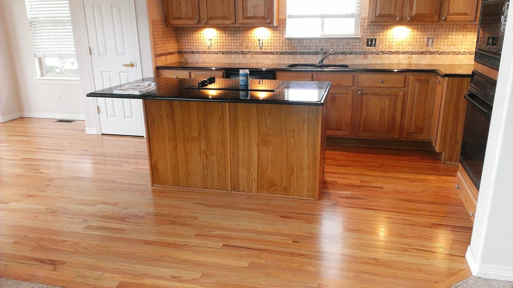An open kitchen and living space after a whole-house remodel, with an island and hardwood flooring