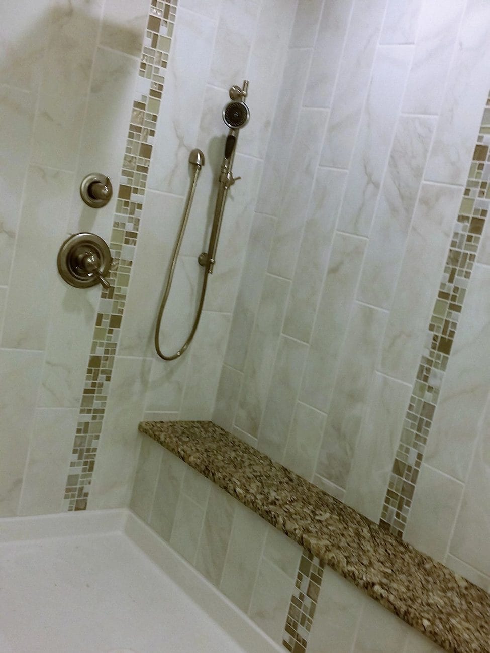 A tiled shower with a stone bench and a mosaic inlay