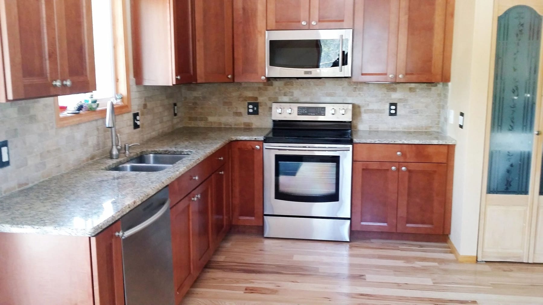 A finished kitchen with cherry cabinets, granite counters and a stone tile backsplash